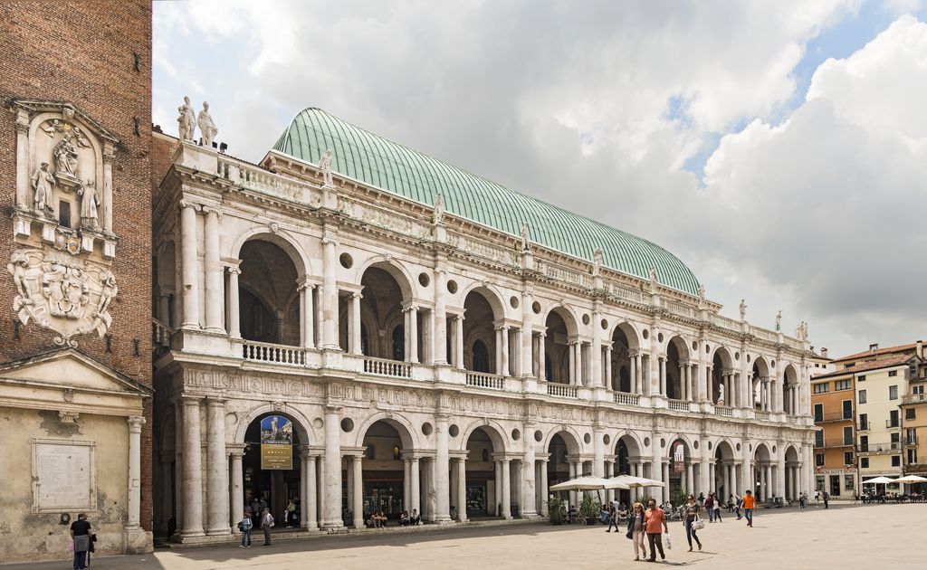 Two long storeys of pale stone arches, paired smaller openings and round columns line a busy square beneath a large green copper roof.