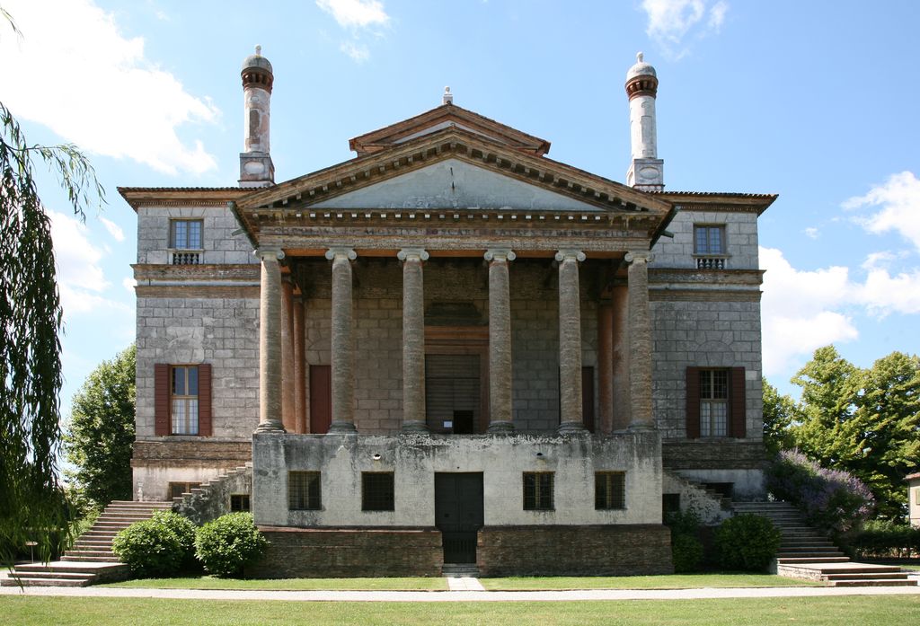 A six-column temple portico and broad pediment stand above a tall weathered base, with paired stairs and square residential wings on either side.