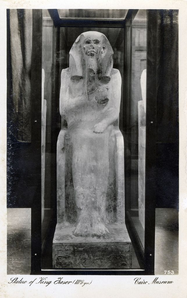 An old black-and-white albumen print shows a damaged life-size seated statue of a king inside a glass museum case, with a handwritten English caption below.