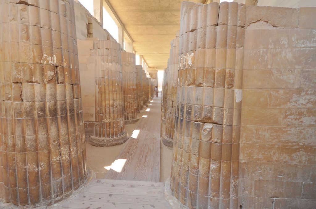 Rows of thick limestone columns carved with vertical bundled-stem grooves flank a narrow roofed passage leading toward a bright opening.
