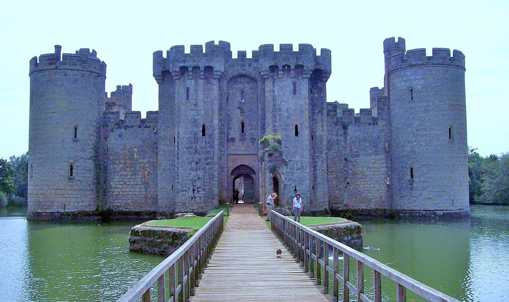 A narrow bridge leads across water to a fortified entrance between stone towers.