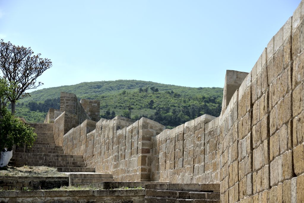 Stone steps ascend beside a crenellated masonry parapet with a wooded hill beyond.