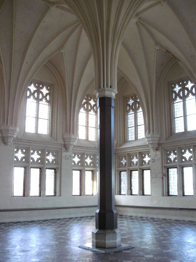 Ribs spread from a central stone support above a large open room lined with windows.