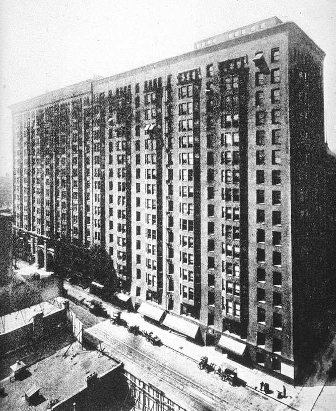 A grainy elevated view shows a long, dark, repetitive masonry office block with rounded corners, many windows, street awnings and traffic.