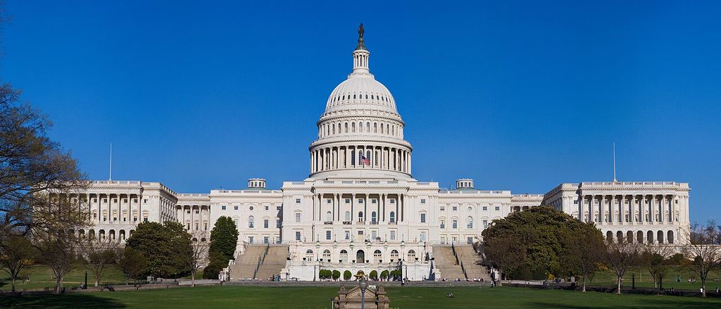 A domed central building and long columned wings stand beyond a lawn and broad approach.