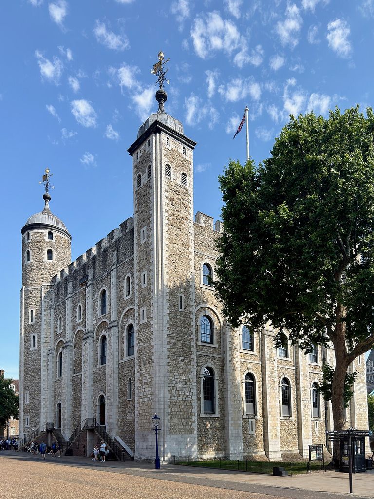A tall rectangular stone keep with corner turrets rises above surrounding grounds and later fittings.