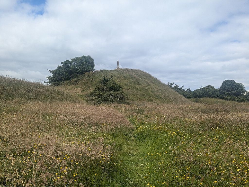 A grassy and partly scrub-covered mound carries a small monument at its top.