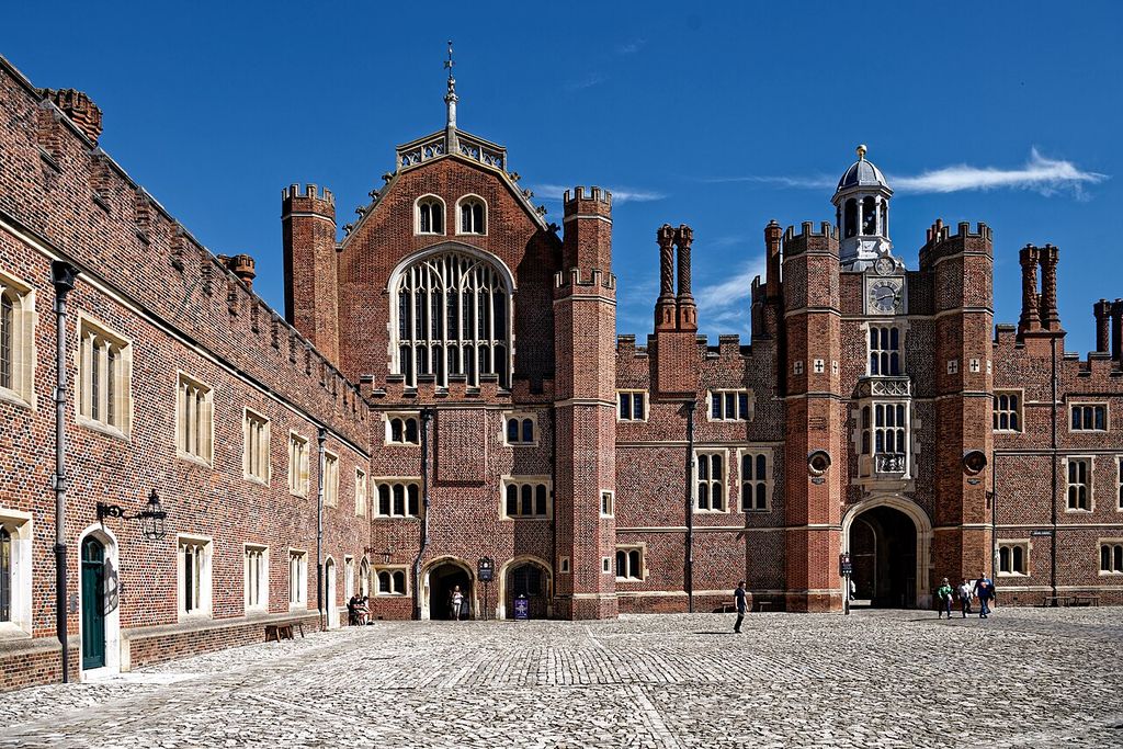A broad cobbled court is enclosed by patterned brick ranges, a great hall façade, clock gateway, towers, chimneys and several visitors.