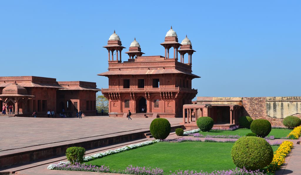 A square red-sandstone pavilion with projecting eaves and four rooftop chhatris stands across a broad court and clipped garden.