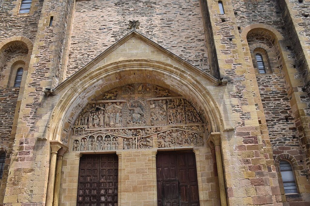 Rows of carved figures fill a rounded tympanum above the upper portions of two doors within deep stone arches.