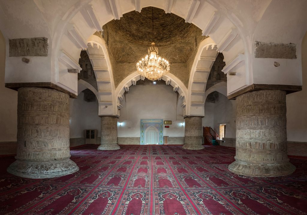 White pointed arches rise from four massive carved stone supports below patterned brick domes and a central chandelier.