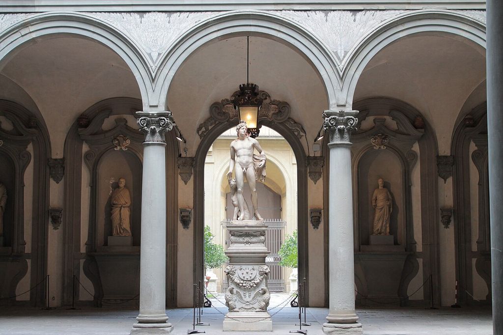 Three broad round arches spring from columns across a courtyard wall, with a passage visible behind a central statue and hanging lamp.