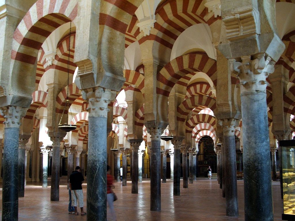 Slender reused columns carry striped lower horseshoe arches and upper round arches repeated through the prayer hall, with visitors and modern fittings below.