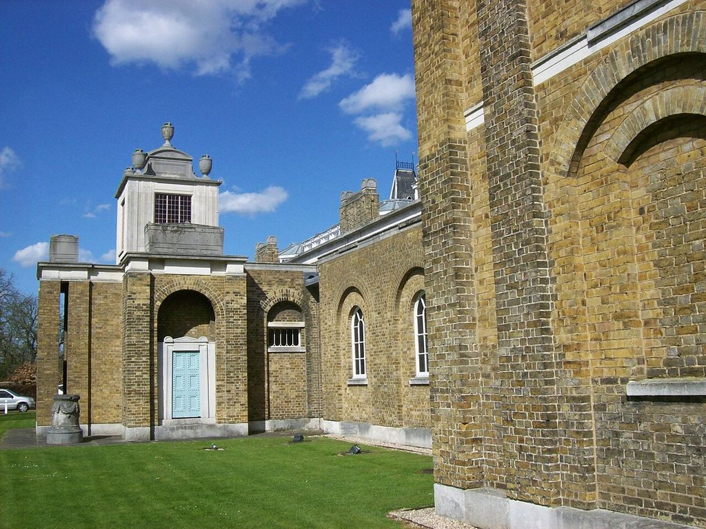 An oblique brick elevation uses repeated recessed round arches, some left as solid wall and others containing doors or windows beneath pale stone bands.