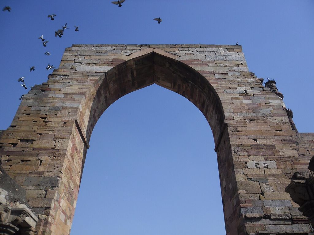 Horizontal stone courses frame a tall pointed opening viewed upward from behind.