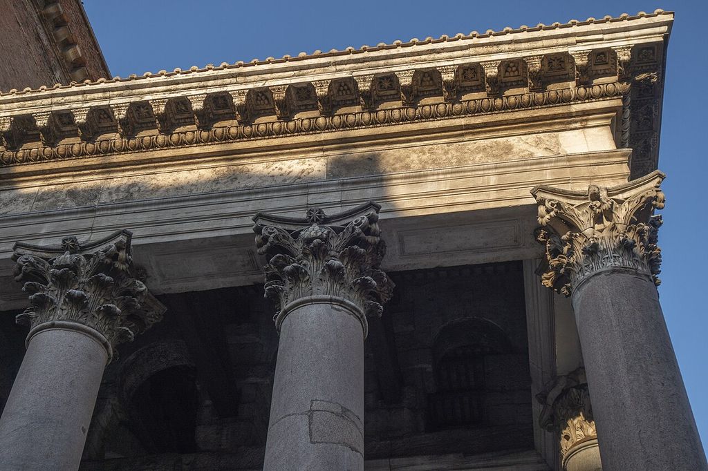 Leaf-covered capitals with small corner scrolls stand above smooth shafts below a projecting decorated cornice.