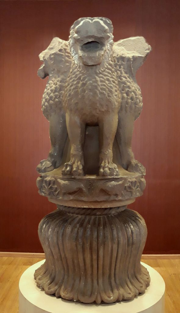 Four lions stand back to back on a circular abacus above a deeply fluted bell-shaped lower member in a museum display.