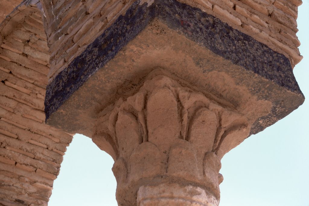A carved stone capital supports a broad square impost block beneath a brick arch, seen closely from below.