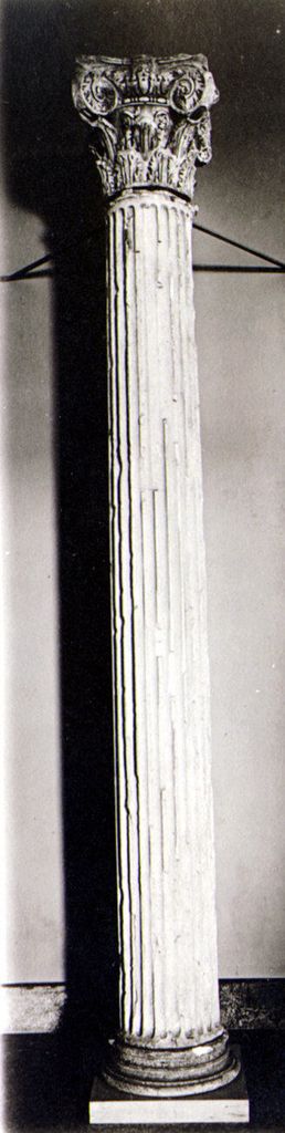 A narrow monochrome museum photograph shows a full fluted column with a leafy capital dominated by large Ionic-like scrolls.