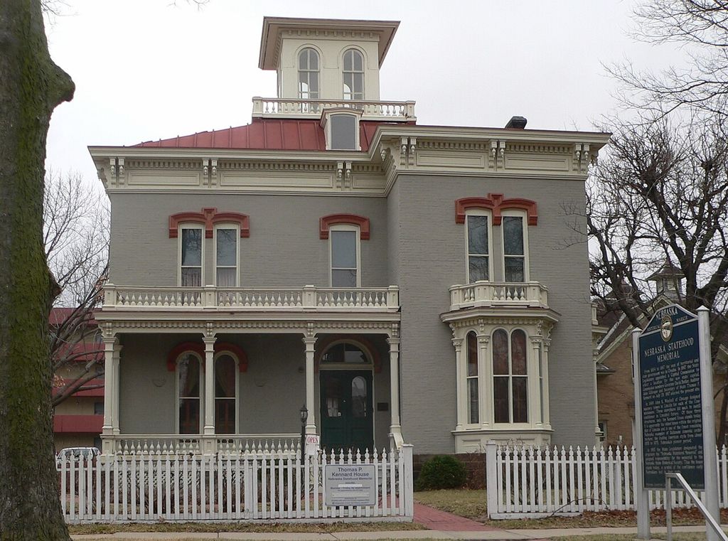 A square windowed rooftop pavilion with a broad overhanging cornice rises above an asymmetrical grey Italianate house.