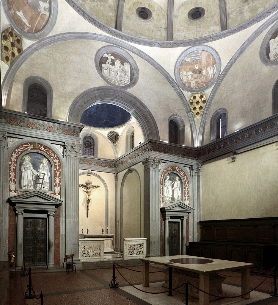A pale ribbed dome rises above curved triangular pendentives, painted roundels, grey stone arches and a square Renaissance chapel interior.