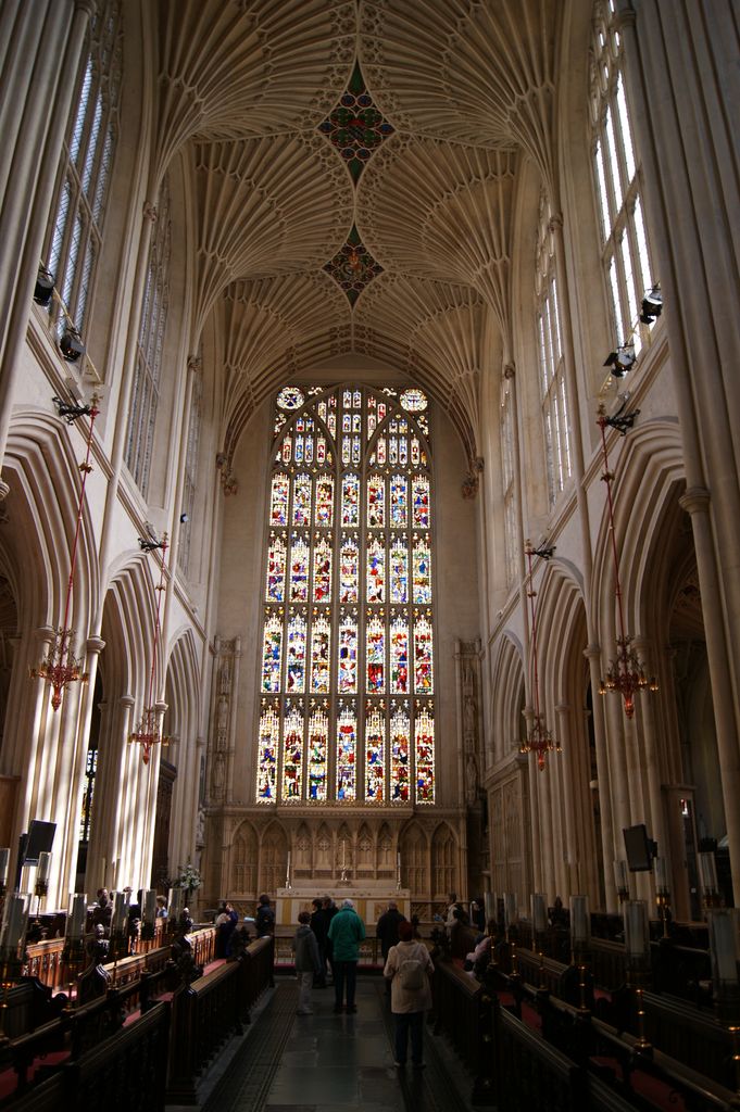 Repeated pale fan vaults and coloured lozenge fields cover the tall chancel above choir stalls and a large stained-glass east window.
