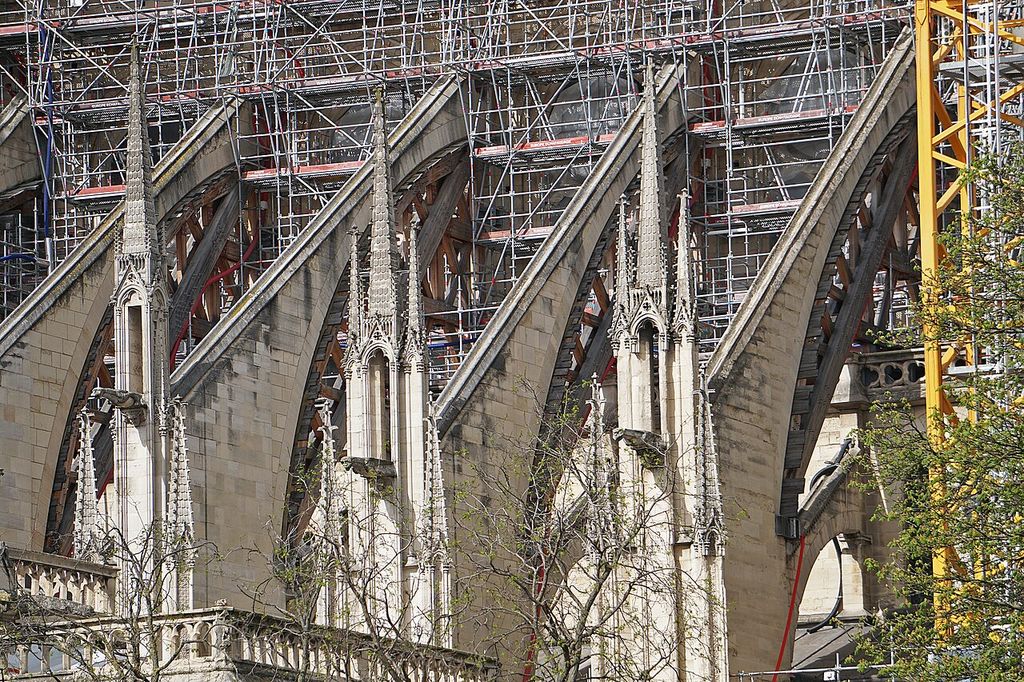 Timber frames fit under the stone flying buttresses beside pinnacles and dense metal scaffolding.