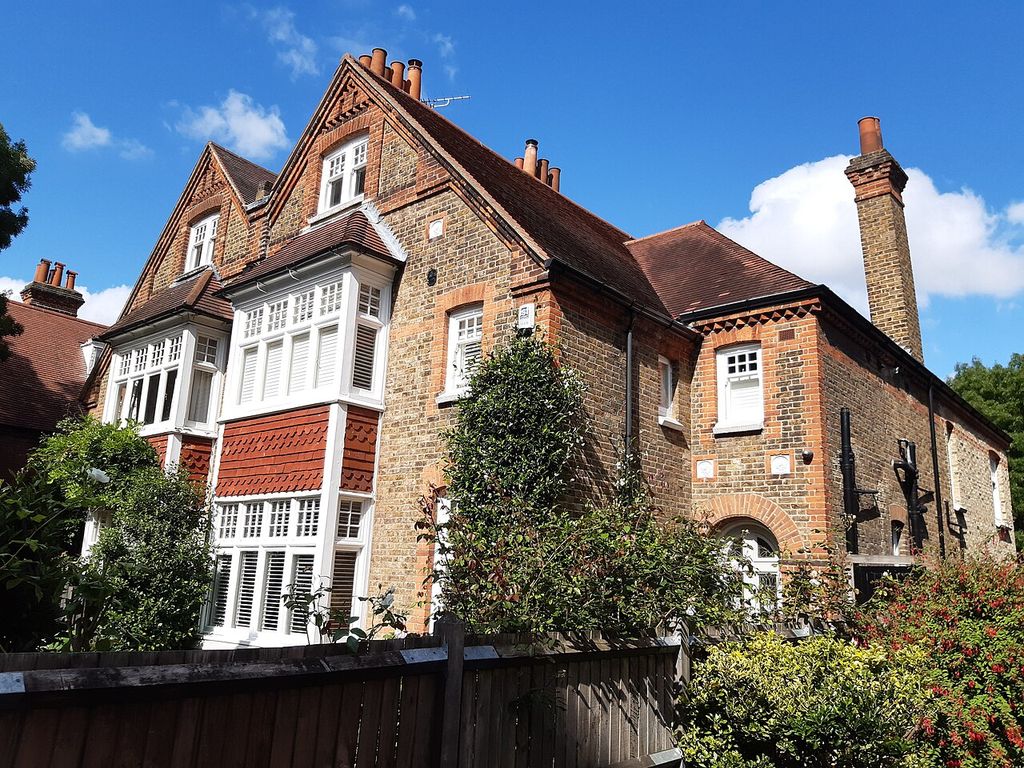 Two large brick gables face a garden above projecting white bay windows, with further pitched roof volumes and tall chimneys behind.