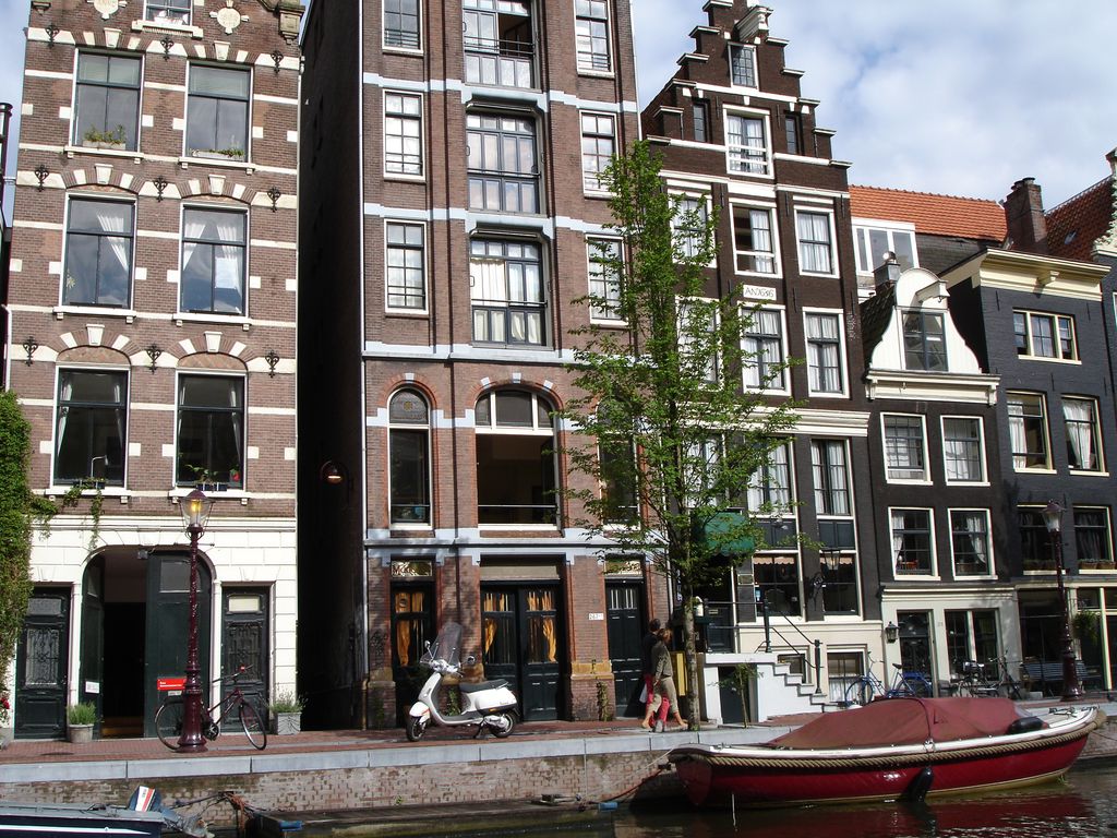 Tall narrow brick canal houses present stepped, neck-like and curved gables above ranked windows, doors, bicycles and a moored boat.