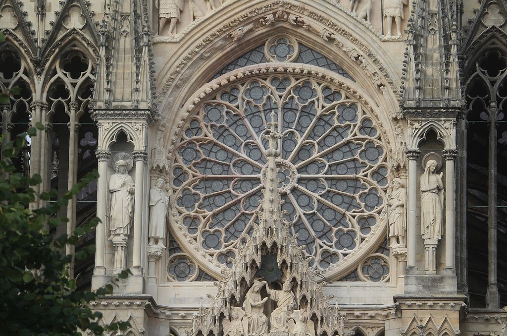 A large circular stone rose with radiating bars and foils sits within a pointed arch above carved figures and openwork niches.