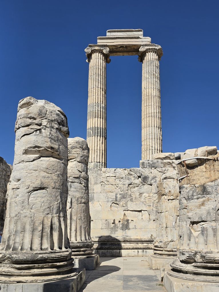 Two tall fluted columns and their architrave rise above massive fallen bases and blocks at Didyma.