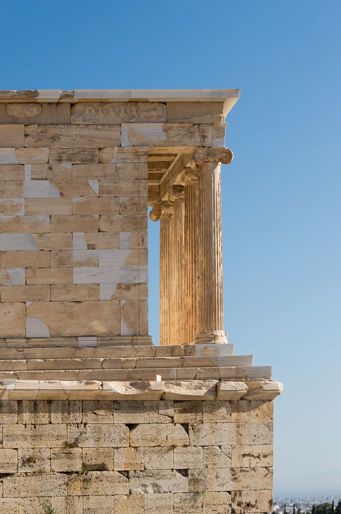 A small marble temple stands above a bastion, with two Ionic columns, its cella wall and many pale restoration patches visible.