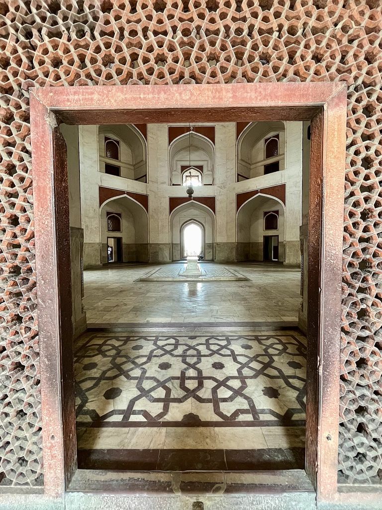 The image captures the beautiful geometric lattice work (jali) framing the view into the main hall of the tomb.
