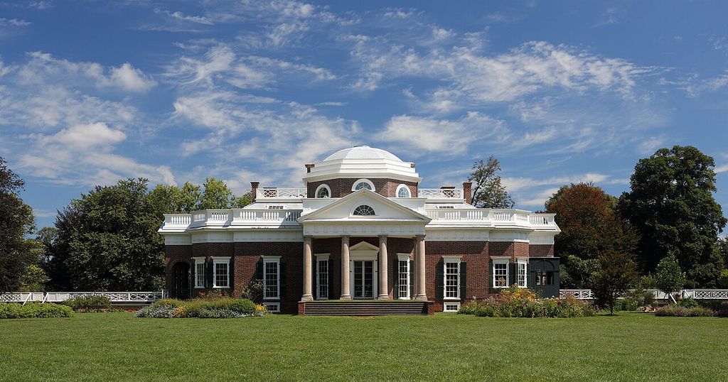 A compact columned portico and triangular pediment stand at the centre of a red-brick house below a low white dome.