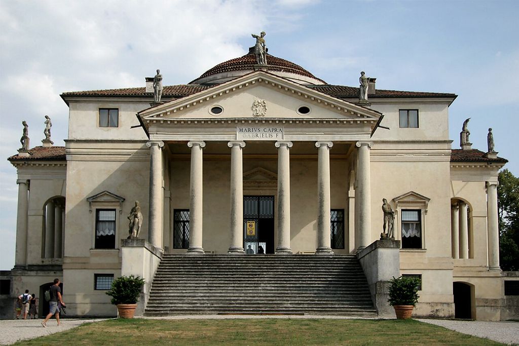 A broad stair rises to six columns and a triangular pediment on a symmetrical pale villa, with a dome visible above.