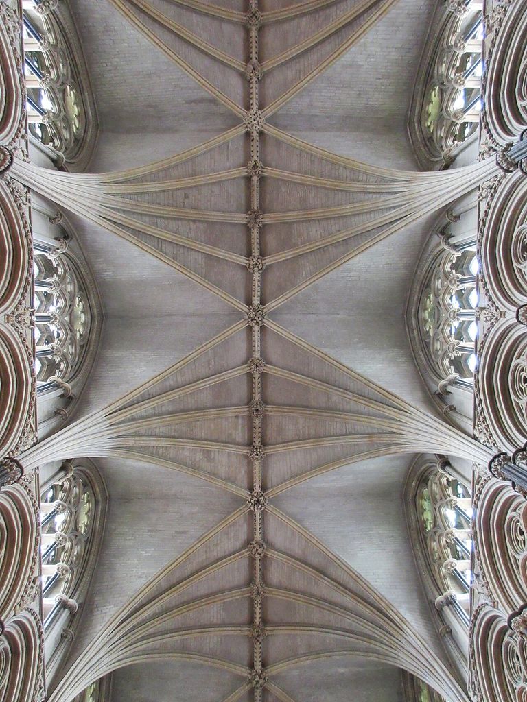 Repeated diagonal and ridge ribs meet at many carved bosses across a pale stone choir ceiling between high windows.