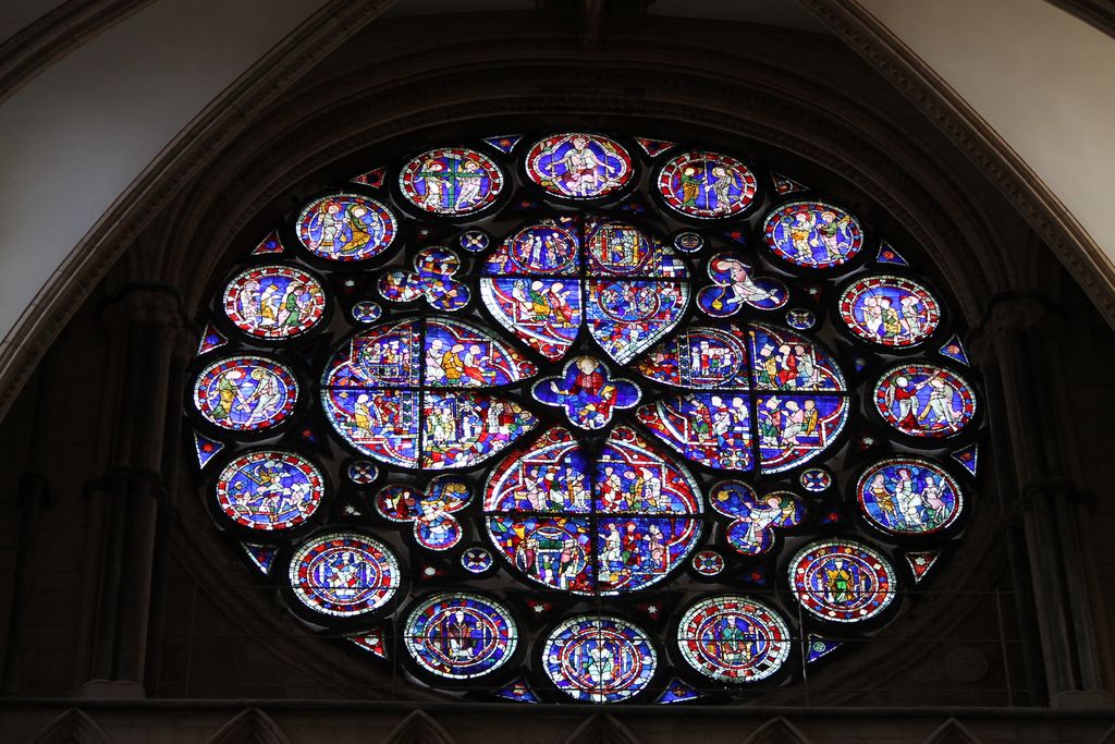 A circular stained-glass window contains broad figurative lobes, coloured perimeter medallions and smaller foils within a dark stone ring.