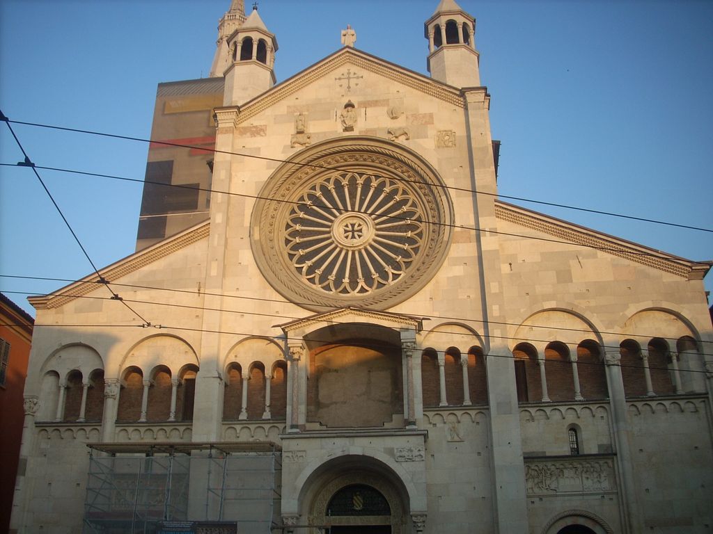 A pale gabled cathedral façade contains a large circular wheel window with many simple spokes above arcades and portals.