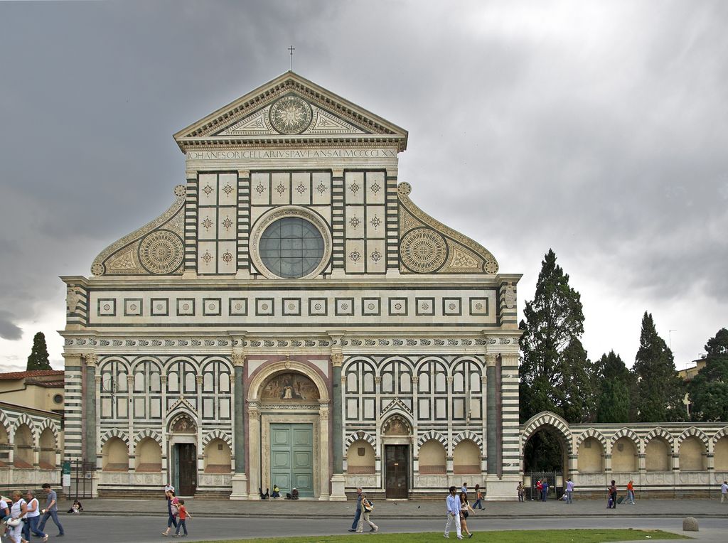 A symmetrical green-and-white marble façade surrounds a large gridded circular window above three portals and a public square.