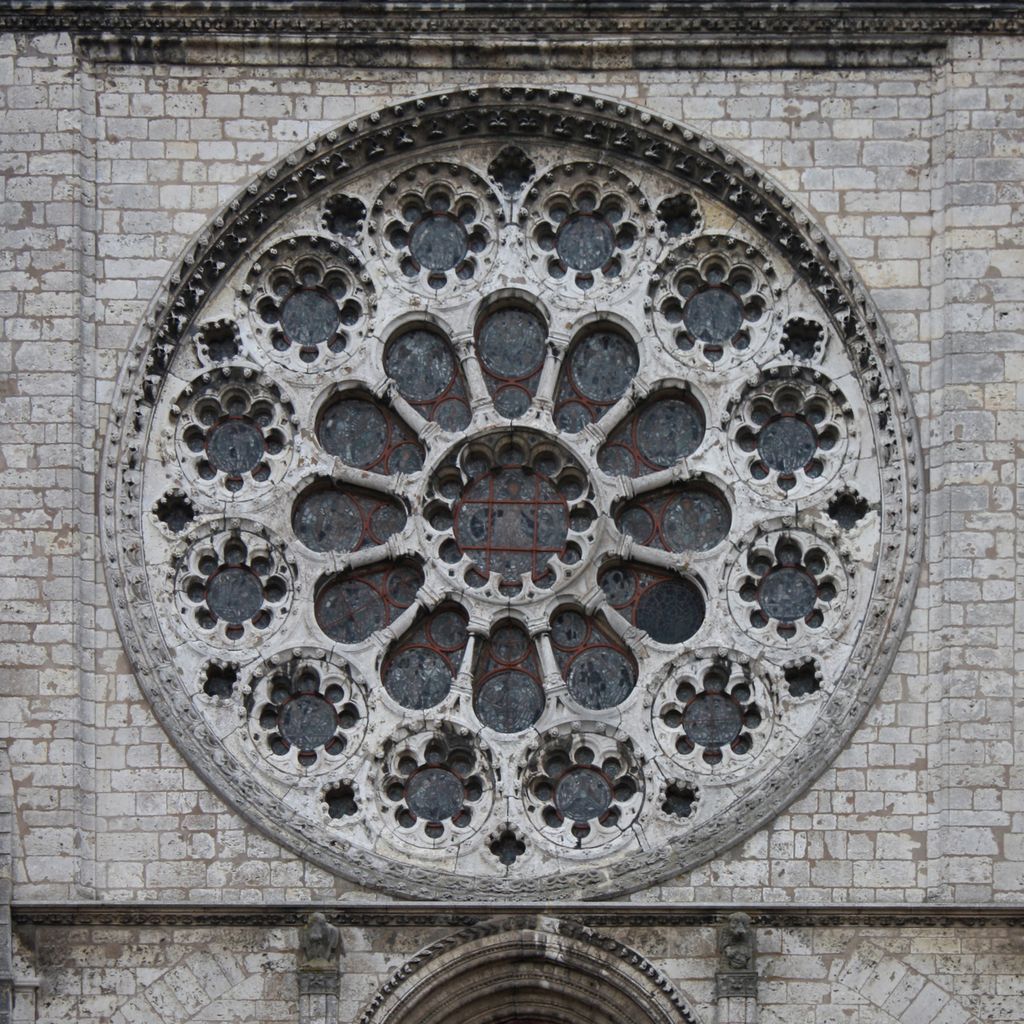 A circular stone window contains nested round and foil-shaped openings around a central glazed circle within pale jointed masonry.
