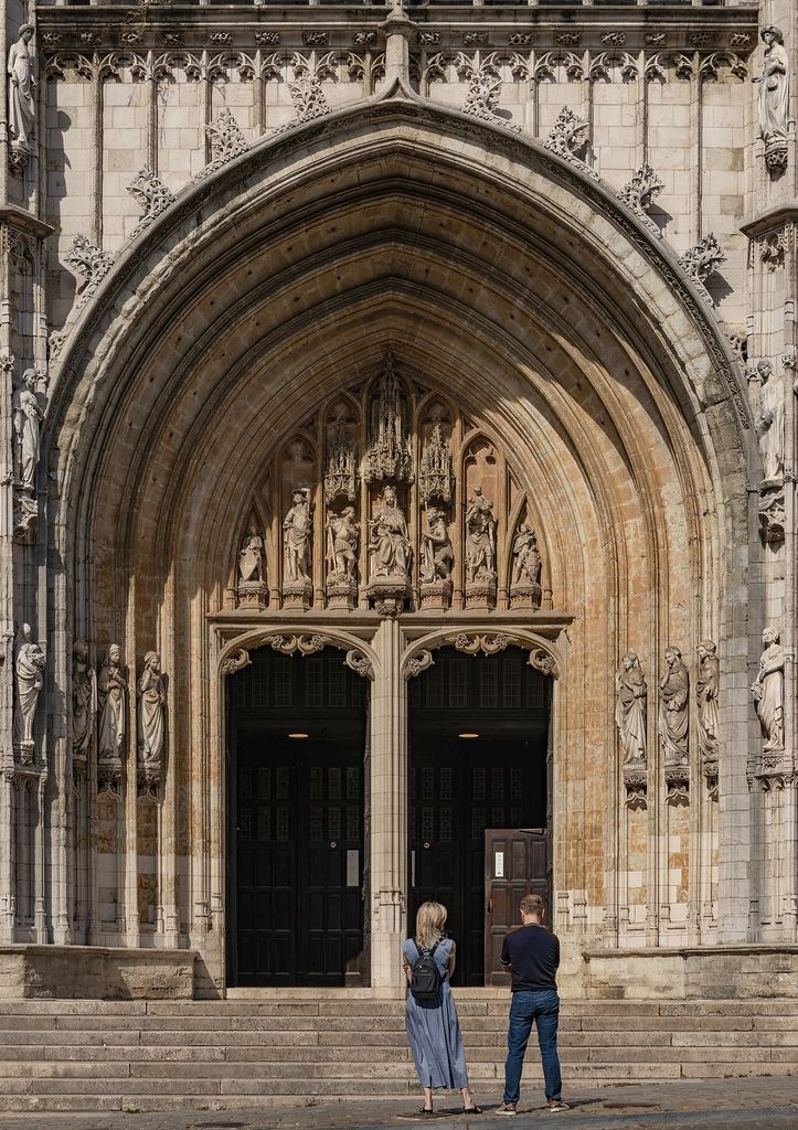 Symmetrical view of the main pointed arch entrance portal showing the stone tympanum sculptures and two visitors standing on the steps.