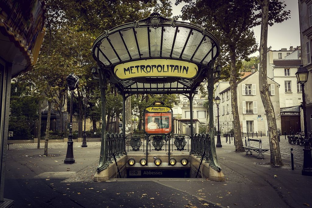 Curving metal supports and a glazed canopy frame the Métropolitain sign above stairs descending into Abbesses station.
