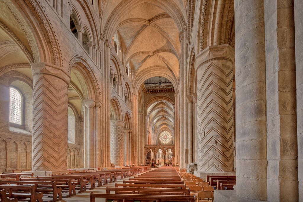 Patterned stone piers and round arcades beneath the rib-vaulted nave of Durham Cathedral, with rows of wooden pews.