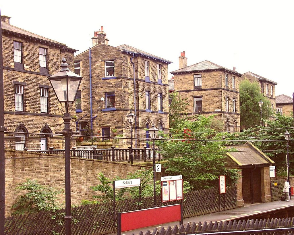 Rows of stone workers’ houses with repeated sash windows and chimneys behind Saltaire railway platform.
