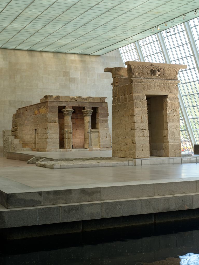 Sandstone gateway standing before the columned Temple of Dendur inside a glazed museum gallery.