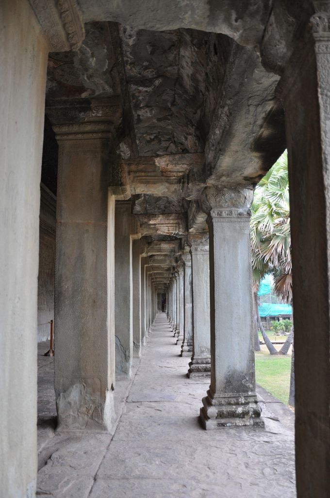A narrow stone gallery recedes through repeated square columns beneath a heavily weathered roof of projecting stone courses.