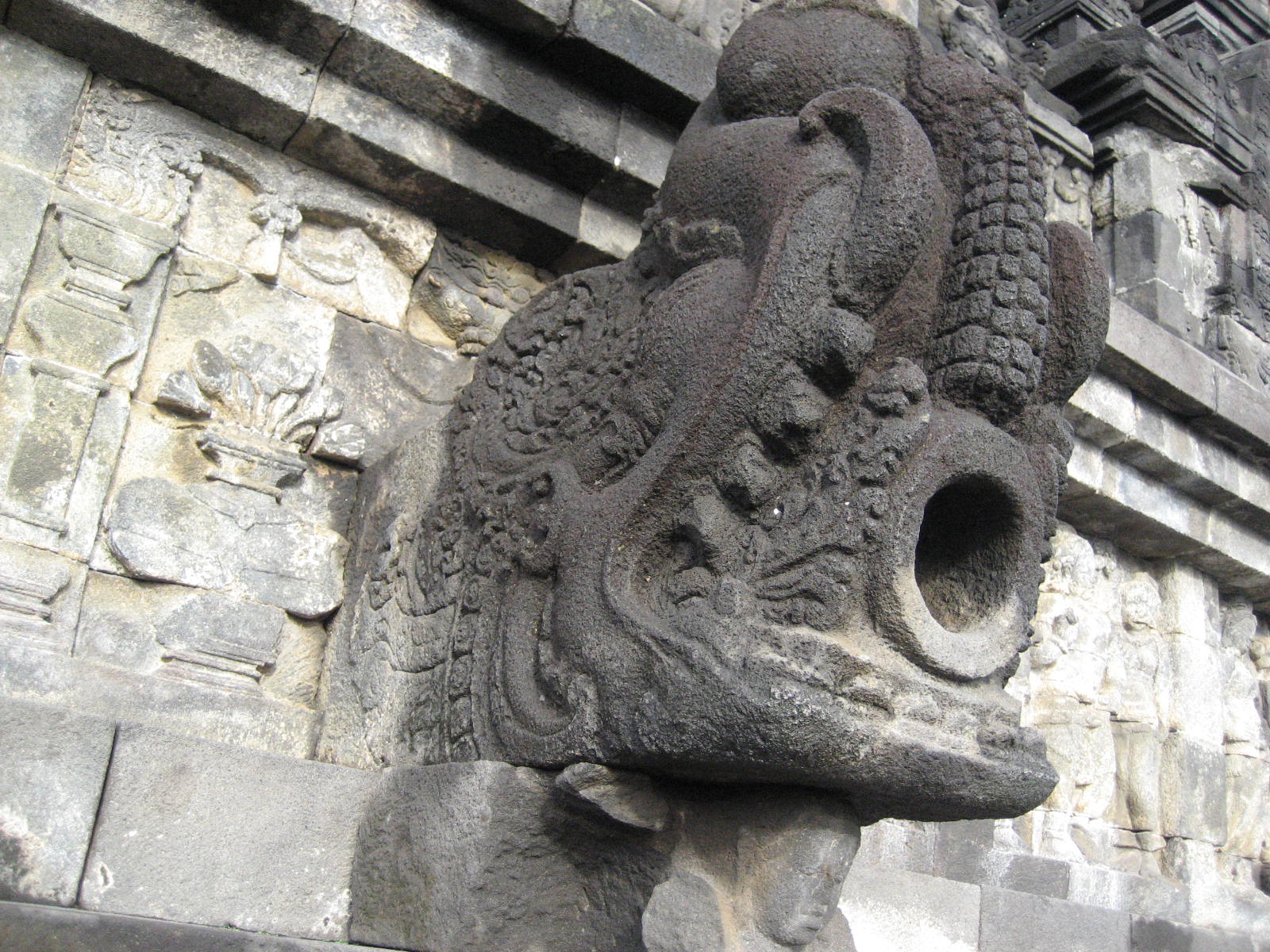 In-situ sculpted animal-head water outlet projecting from Borobudur stone masonry, with its hollow channel visible.