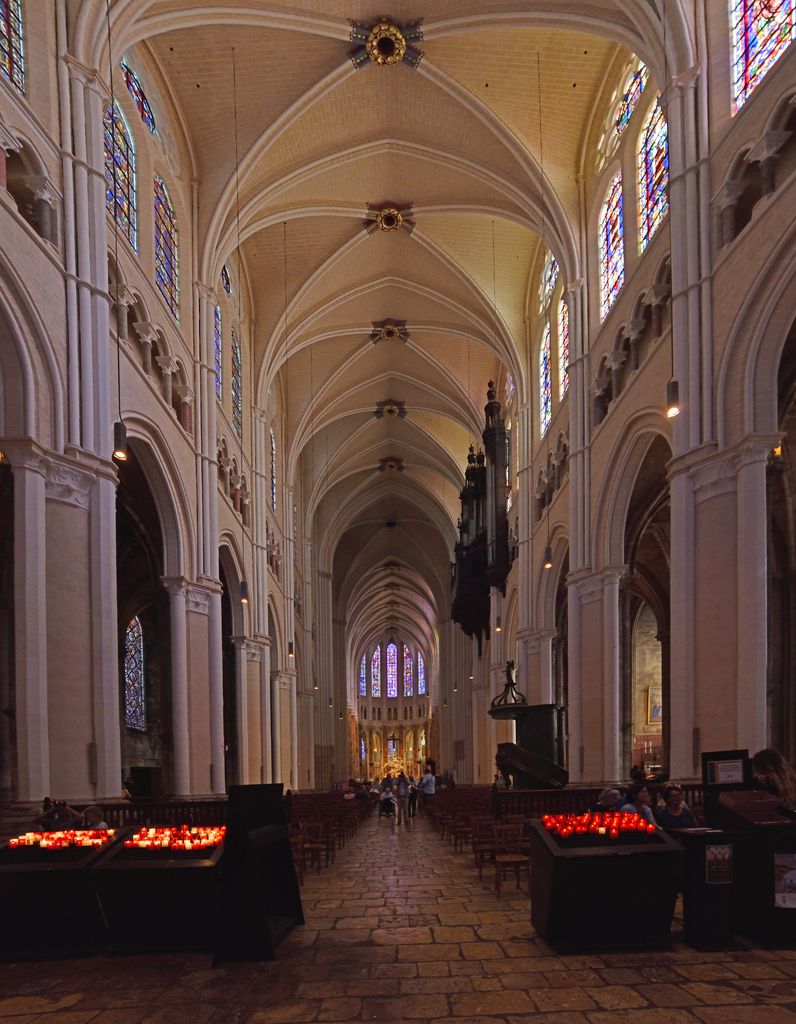 A long cathedral nave has tall pointed arcades, a narrow middle gallery, paired stained-glass windows and pale four-part rib vaults extending toward the choir.