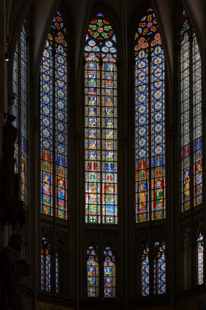 Tall stained-glass royal figures stand beneath painted canopies in the central clerestory windows of Cologne Cathedral’s choir.