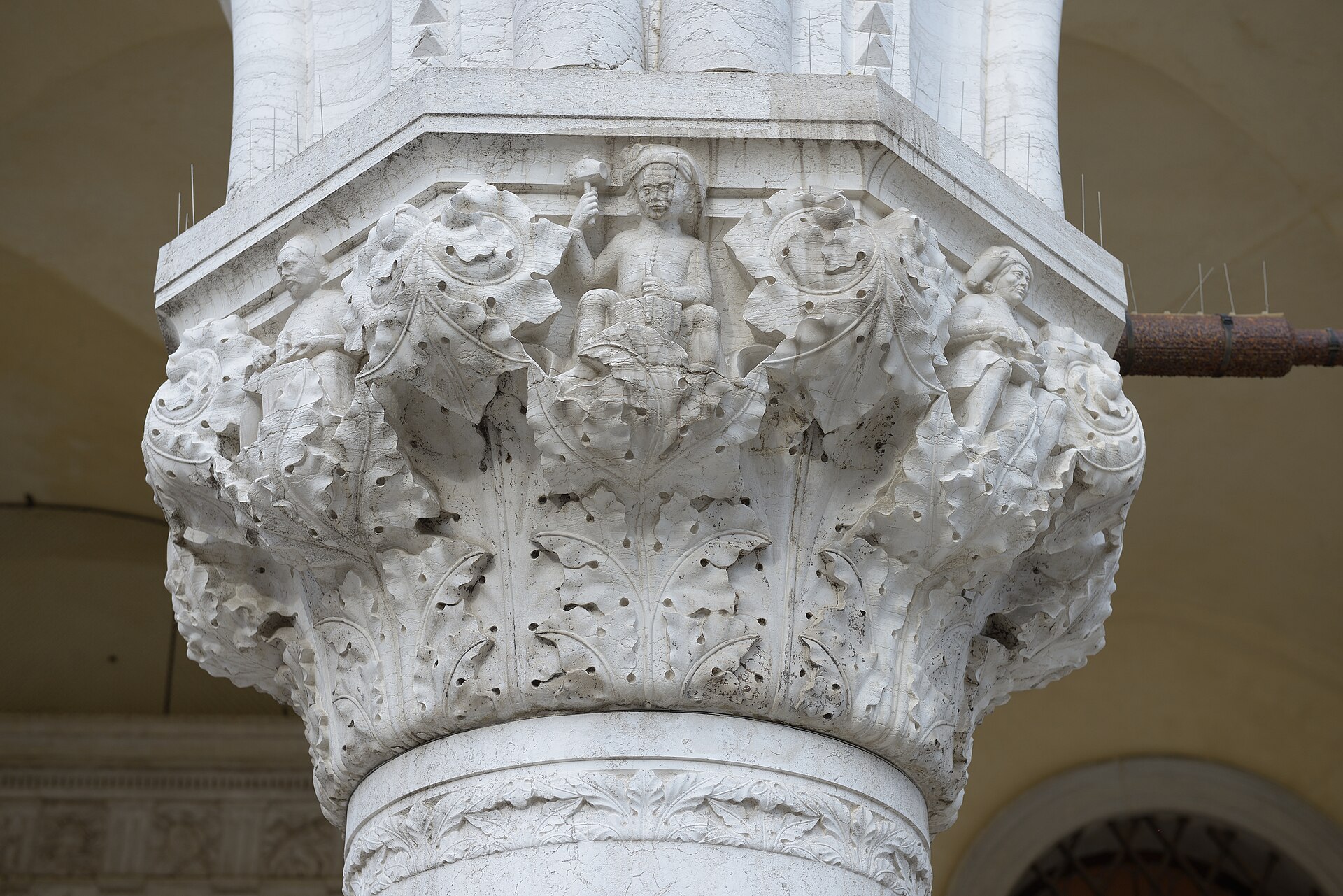 Carved stone worker on the Capital of Trades at the Doge’s Palace, holding tools amid Gothic foliage.